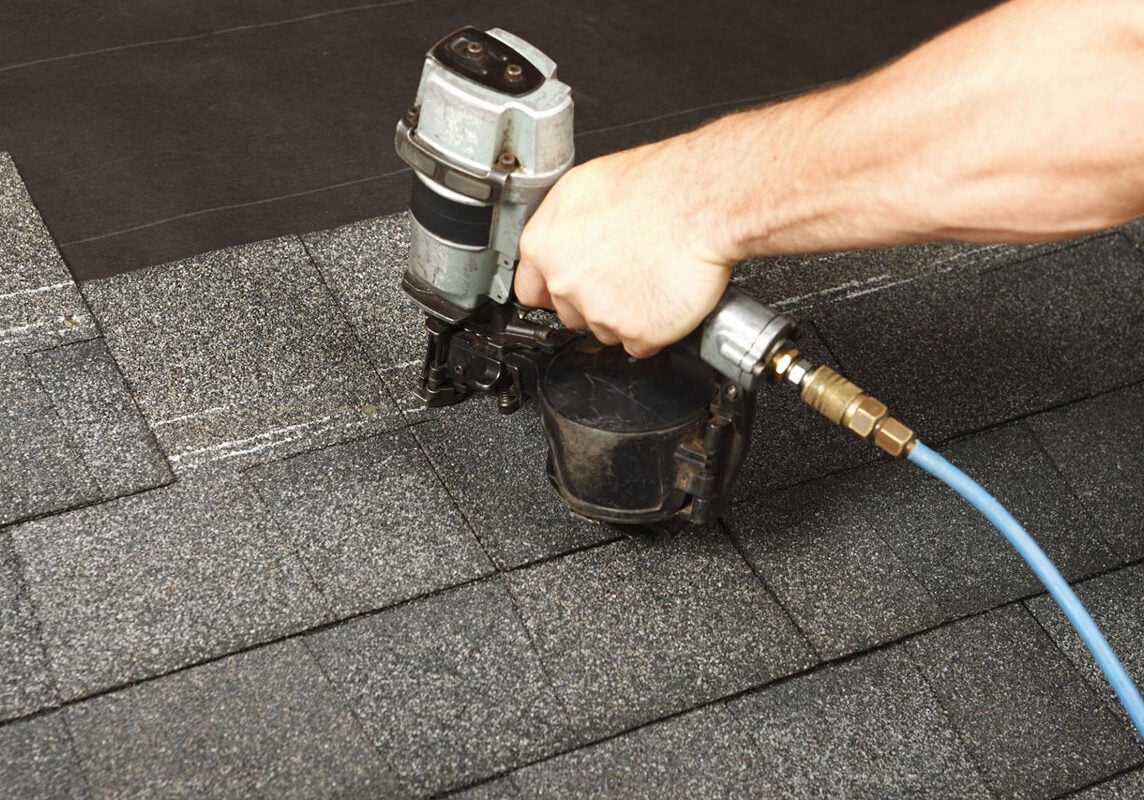 Roofing nailer in use on shingles A person using a roofing nailer on shingles. The tool is connected to a blue hose.