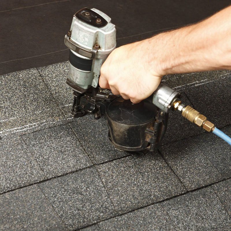 Roofing nailer in use on shingles A person using a roofing nailer on shingles. The tool is connected to a blue hose.