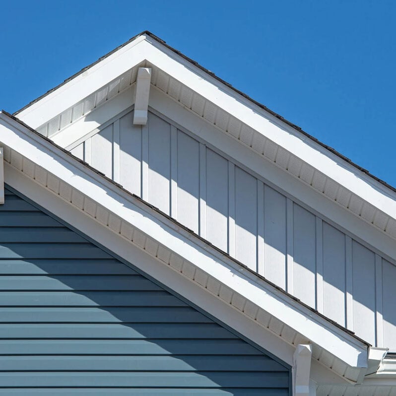 Roof of house with blue siding and white trim A house roof with blue siding and white trim under a clear blue sky. The roof has a gable design with white eaves.