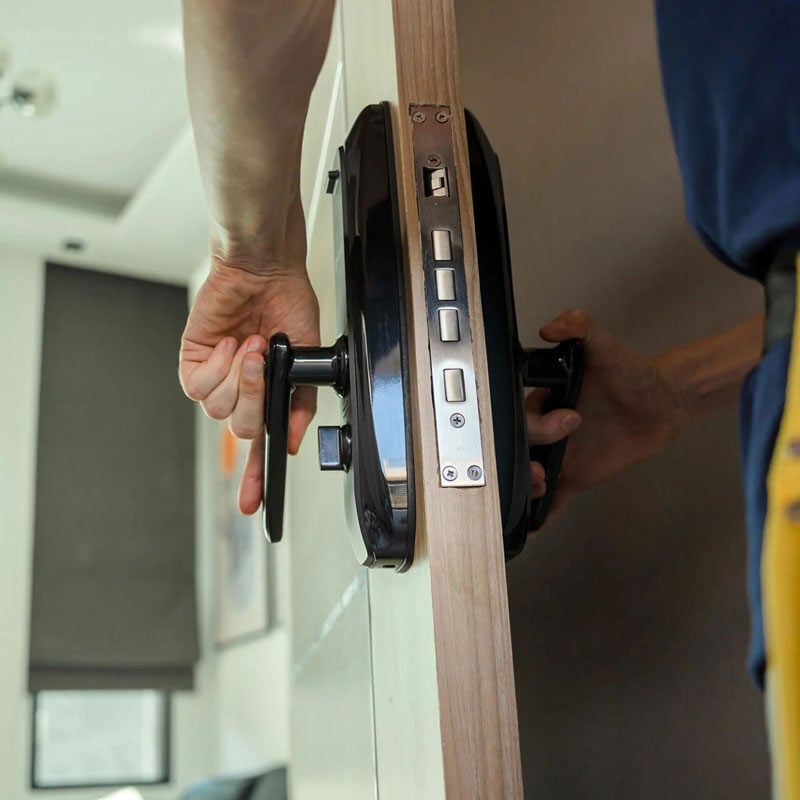 Installing smart lock on wooden door Person installing smart lock on door. The device has a digital keypad.