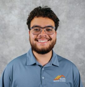 A man with curly hair and a beard wearing glasses and a blue polo shirt with a logo.