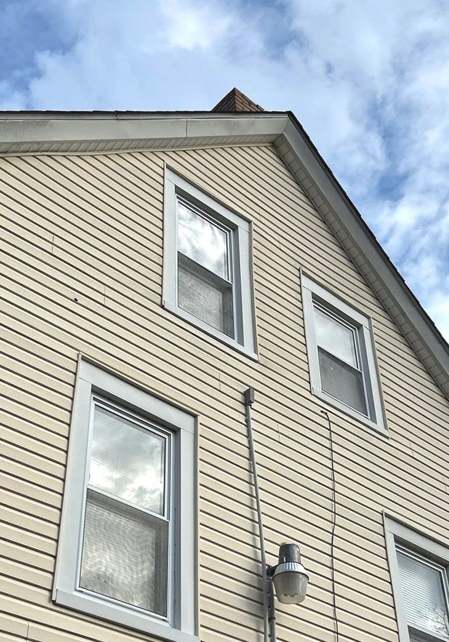 A tan house with white window frames. The house has a cloudy blue sky in the background.
