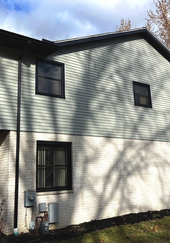 A two-story house with gray siding and white trim. The house has several windows.