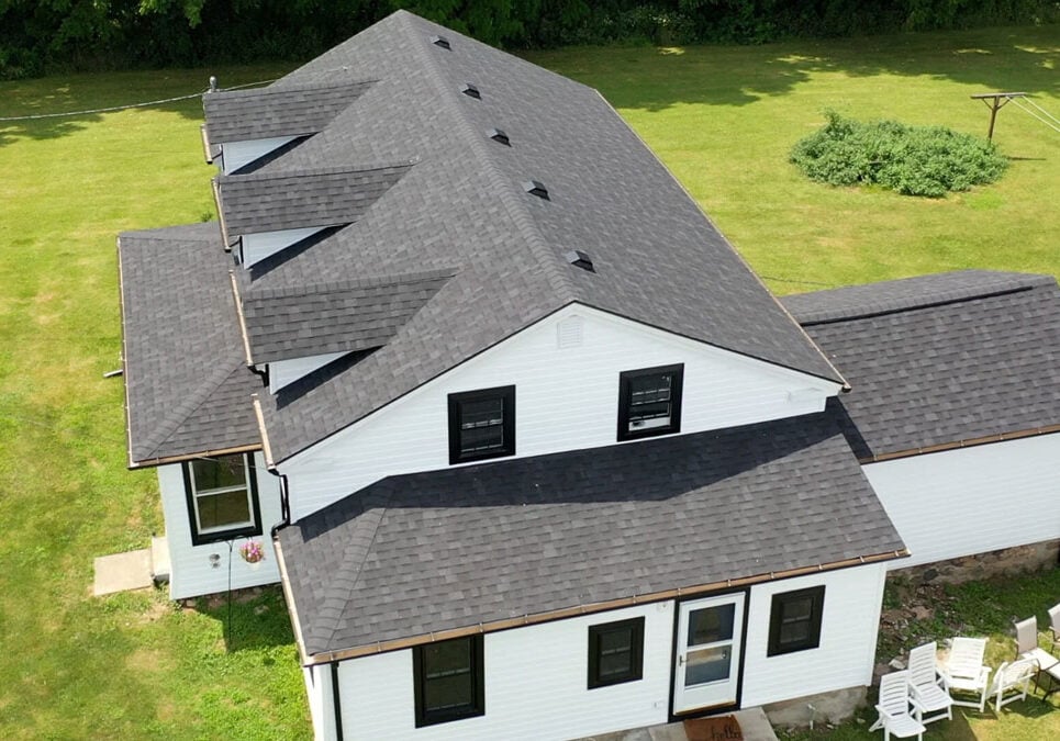 A white house with a gray roof and a green lawn. The house has multiple windows and a patio area.