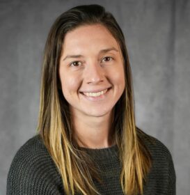 Portrait of a woman with long brown hair. She is smiling and looking at the camera.