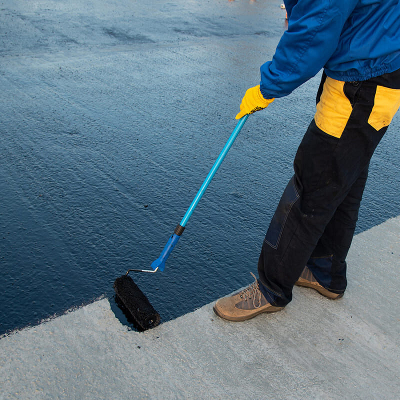 Worker applying sealant to concrete surface A worker in protective gear applying a sealant.